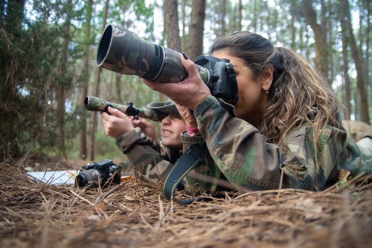 Alt="Absorbed mother and son taking pictures in forest. Family with modern cameras lying on ground, using camera and binoculars."