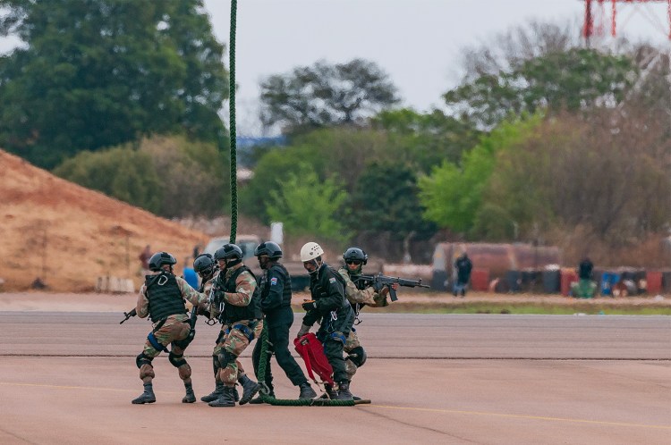 alt=" Armed South African soldiers disembark from Rooivalk helicopter during a battle simulation demonstration at the Africa Aerospace and Defence expo 2024."